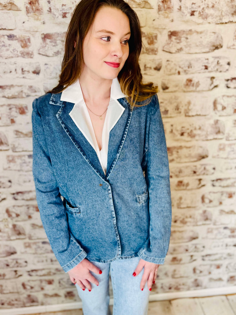 long sleeve denim blazer is single breasted with two front pockets. can be worn as a jacket or blazer. Model is wearing a white collar shirt and denim faded jeans