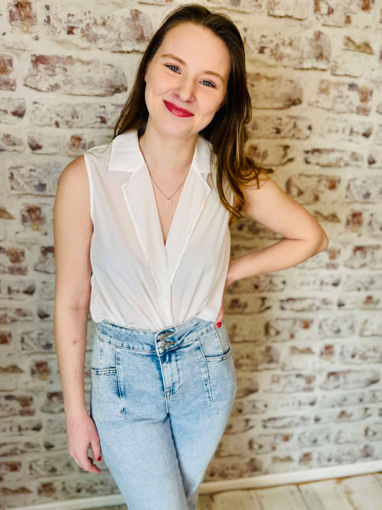 Sleeveless surplice blouse light material is cream colored and the low plunge v- neck lapel lays flat on the blouse.  Model is wearing faded jeans
