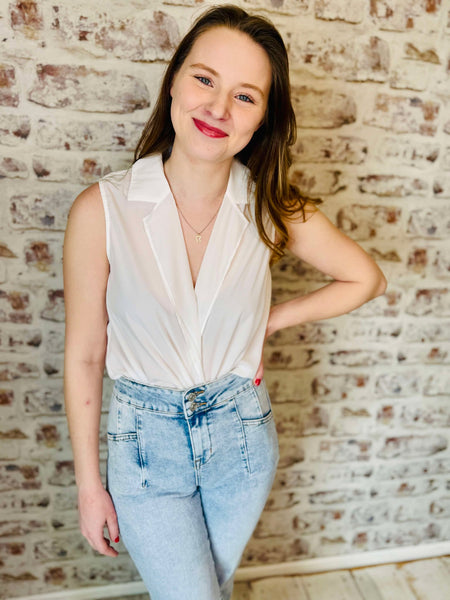 Sleeveless surplice blouse light material is cream colored and the low plunge v- neck lapel lays flat on the blouse.  Model is wearing faded jeans