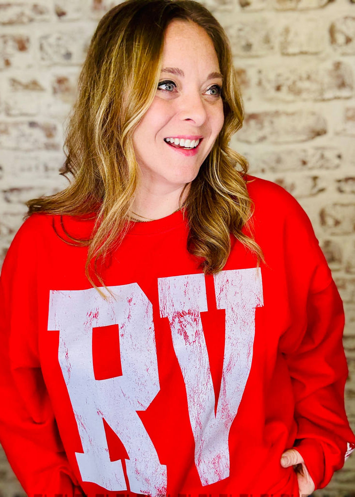 Person wearing a red sweatshirt with 'RV' printed on it against a brick wall.