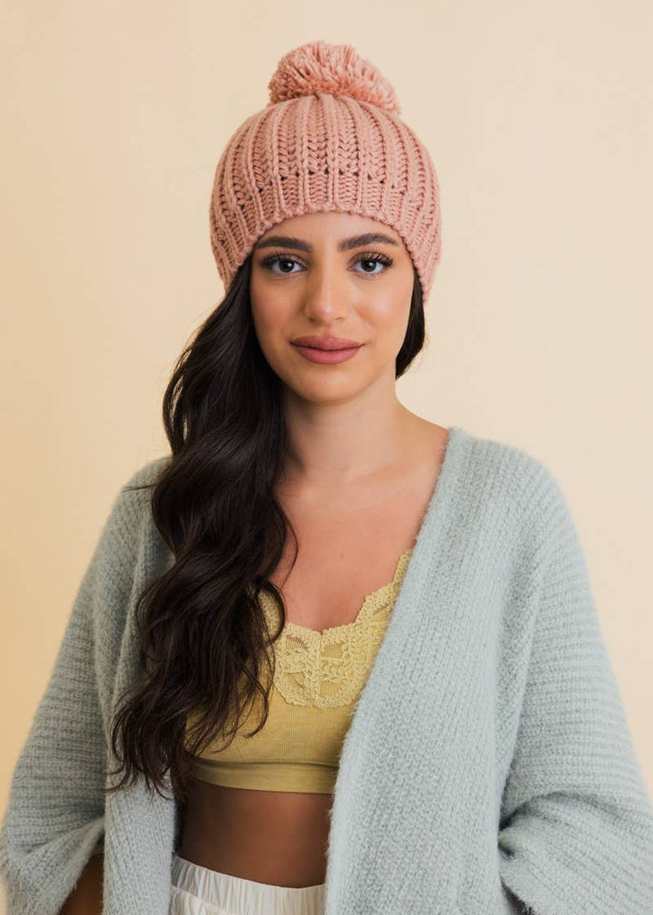 a pink knitted beanie with a yarn pom adorned atop.