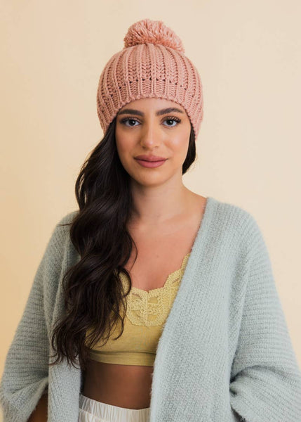 a pink knitted beanie with a yarn pom adorned atop.