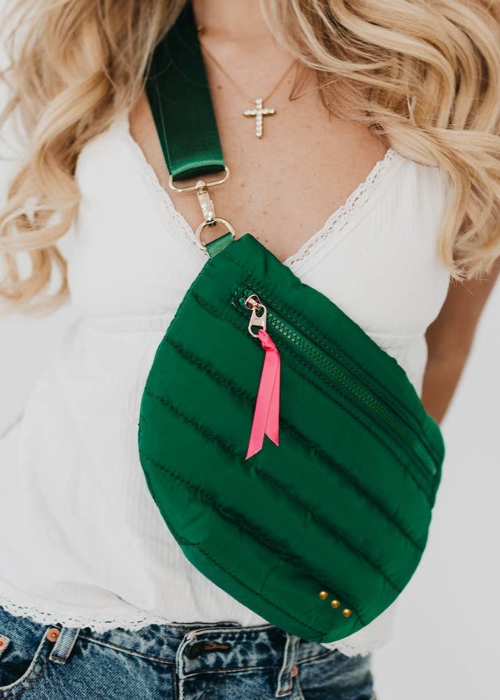 A trendy take on the updated fanny pack that can be worn in multiple ways. Wear it as a belt bag/fanny pack, crossbody, or shoulder bag. Features a fun half moon shape with a coordinating shiny canvas strap and gold hardware and a pop of color with ribbon accent.