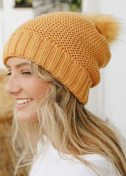 A mustard yellow knit beanie with a pom-sherpa lined hat