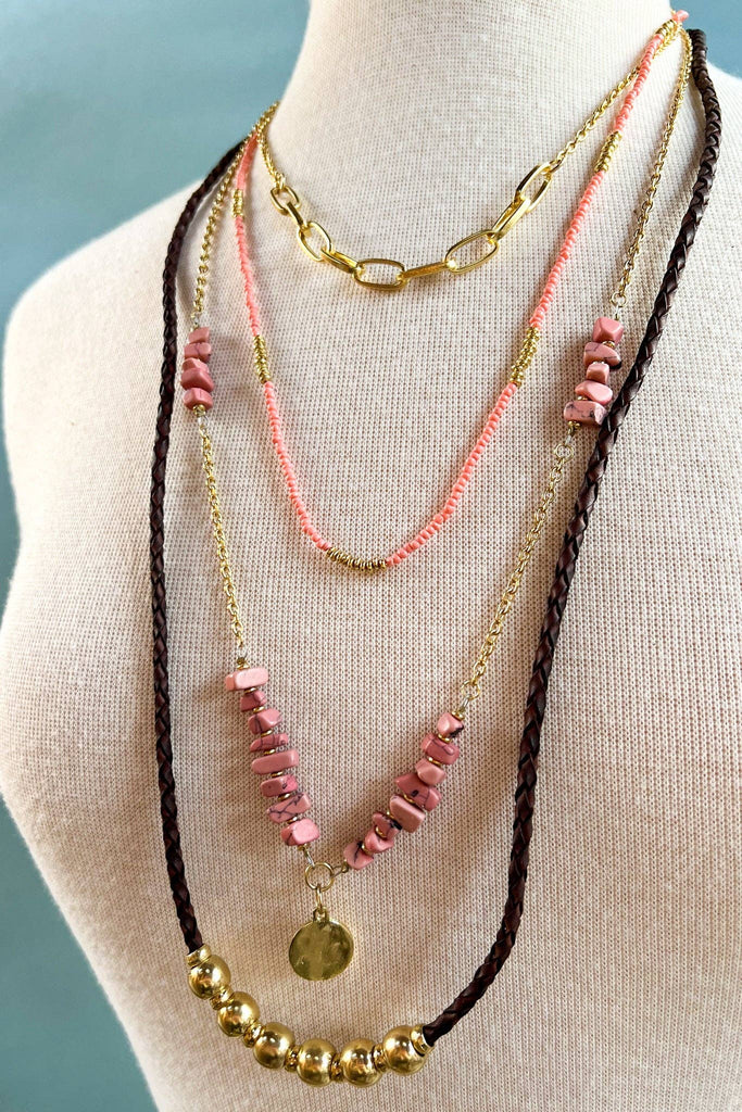 Three necklaces with pink beads and gold accents on a mannequin bust.