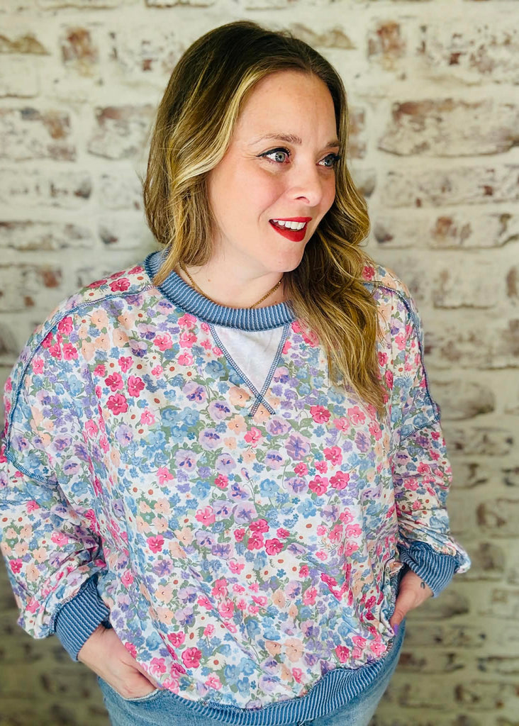 Woman wearing a floral patterned sweater against a brick wall.