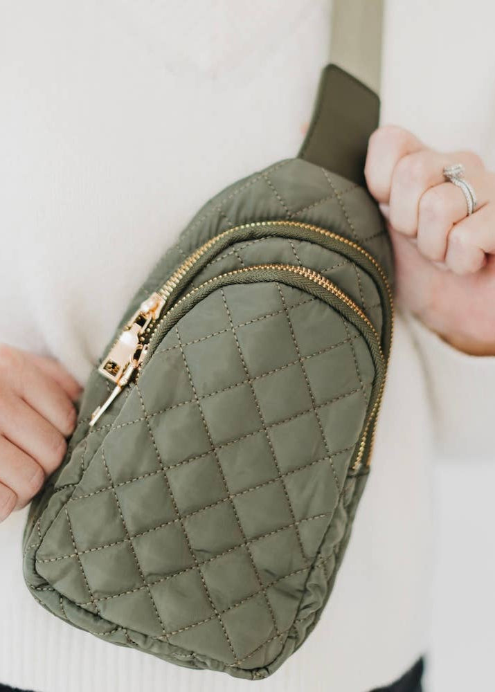 Green quilted fanny pack with gold zipper held by a person wearing a white sweater.