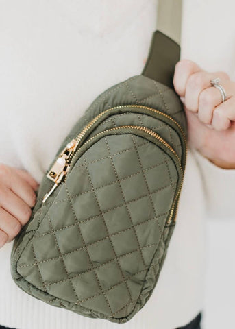 Green quilted fanny pack with gold zipper held by a person wearing a white sweater.